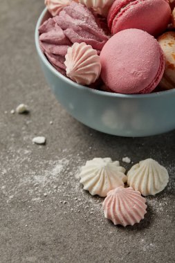 Lezzetli fransız macaroons, yumuşak zephyr ve gri arka plan üzerinde şeker parçaları ile küçük pembe ve beyaz bezeler ile Mavi kase