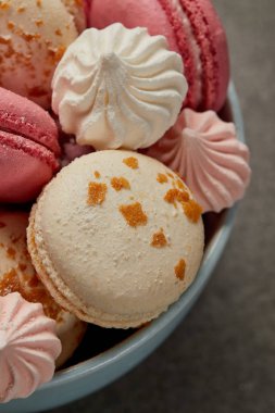 Lezzetli fransız macaroons, yumuşak zephyr ve gri arka plan üzerinde mavi kase küçük pembe ve beyaz bezeler