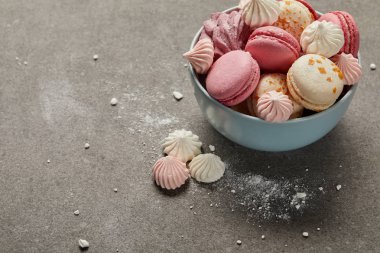 Mavi kase de lezzetli fransız macaroons ve bezeler ve gri arka plan üzerinde şeker parçaları ezilmiş