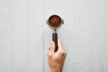 Top view of man holding portafilter with coffee on white wooden surface clipart