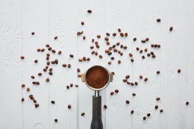 Top view of portafilter with coffee on white wooden surface with scattered coffee beans clipart