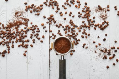 Dağınık kahve çekirdekleri ile beyaz ahşap yüzeyüzerinde öğütülmüş kahve ile portafilter üst görünümü