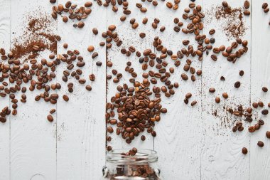 Coffee beans scattered on white wooden surface with glass jar clipart