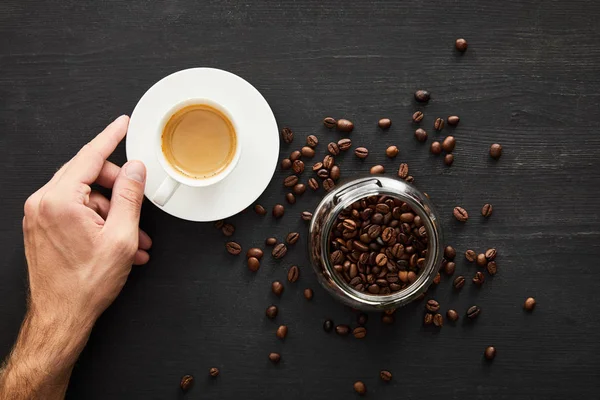 コーヒー豆とガラス瓶の近くにコーヒーのカップと男性の手のトップビュー — ストック写真