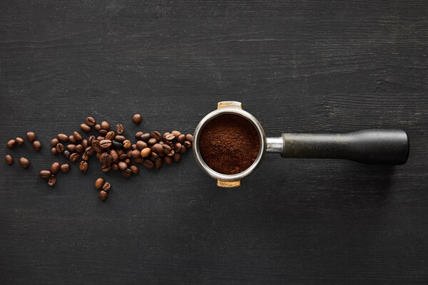 Top view of portafilter with coffee on dark wooden surface with scattered coffee beans