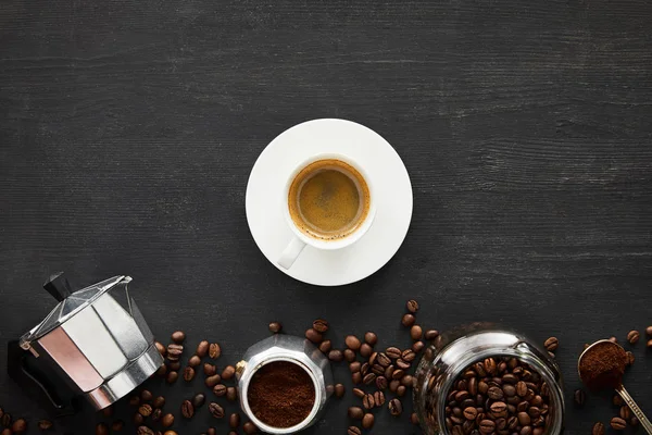 間欠泉コーヒーメーカーの近くのソーサー上のエスプレッソのカップのトップビュー コーヒー豆と暗い木製の表面にガラス瓶とスプーン — ストック写真
