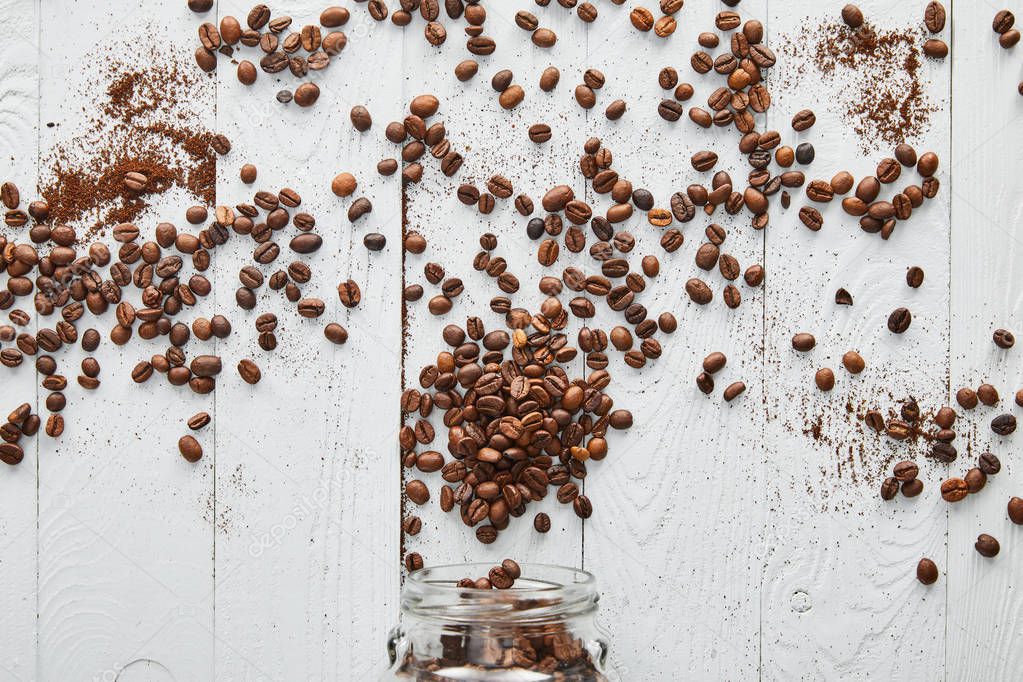 Coffee beans scattered on white wooden surface with glass jar