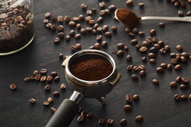 Portafilter kahve çekirdekleri ile koyu ahşap yüzeyüzerinde kaşık ang cam kavanoz yakınında öğütülmüş kahve ile dolu