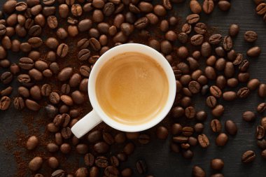 Dağınık kahve çekirdekleri ile koyu yüzeyde espresso ile beyaz fincan üst görünümü