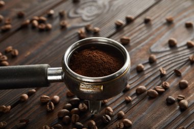 Portafilter filled with fresh ground coffee on dark wooden surface with coffee beans clipart