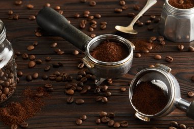 Portafilters near spoon, glass jar and parts of geyser coffee maker on dark wooden surface clipart
