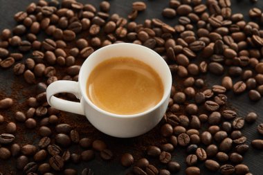 Dağınık kahve çekirdekleri ile yüzeyinde espresso ile beyaz seramik fincan