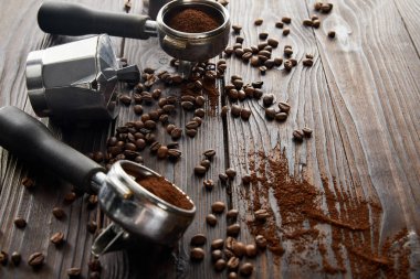 Kahve çekirdekleri ile koyu kahverengi ahşap yüzeyüzerinde portafiltreler arasında Gayzer kahve makinesi