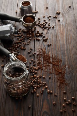 Dark wooden surface with glass jar, portafilters, geyser coffee maker and coffee beans clipart