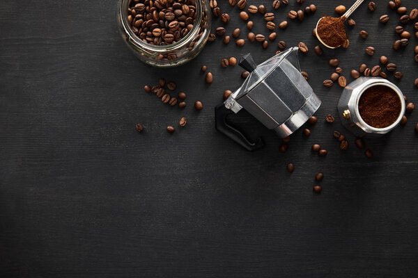 Top view of geyser coffee maker near glass jar and spoon on wooden surface with coffee beans