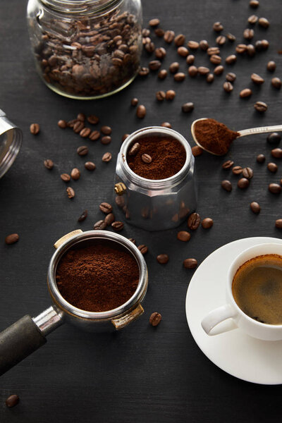 Geyser coffee maker near cup of coffee, portafilter, spoon and glass jar on dark wooden surface with coffee beans