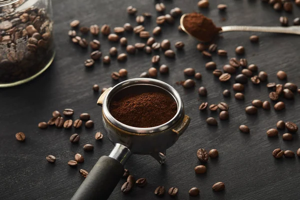 在深色木质表面用咖啡豆在勺子附近加了研磨咖啡的 Portafilter — 图库照片