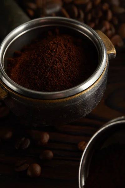コーヒー豆と暗い表面の下に新鮮な挽きたてのコーヒーとポルタフィルター — ストック写真