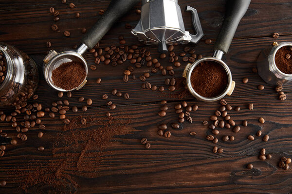 Top view of geyser coffee maker between portafilters and glass jar on dark wooden surface with coffee beans