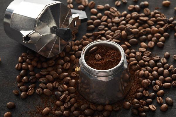 Separated parts of geyser coffee maker with ground coffee on dark wooden surface with coffee beans