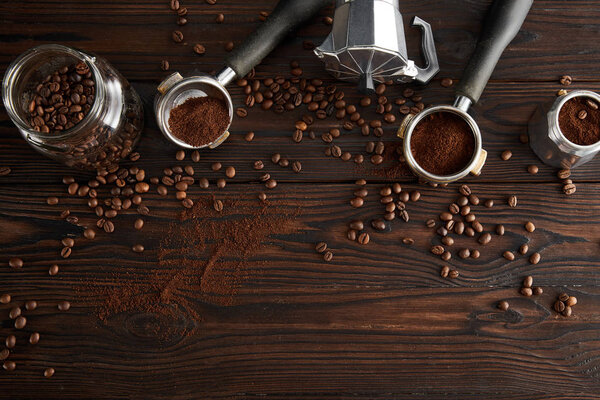 Top view of glass jar near geyser coffee maker and portafilters on dark wooden surface with coffee beans