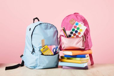 blue and pink backpacks with school supplies near books isolated on pink clipart