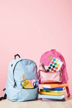 pembe izole kitap yığını yakınında okul malzemeleri ile mavi ve pembe sırt çantaları