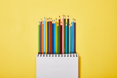 top view of colored pencils near blank notebook on yellow clipart