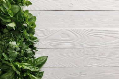 Beyaz beyaz ahşap yüzeyüzerinde taze yeşil fesleğen, kişniş, maydanoz ve nane demetleri üst görünümü