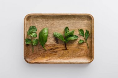 Top view of brown wooden dish with parsley, basil, cilantro and peppermint leaves on white surface clipart