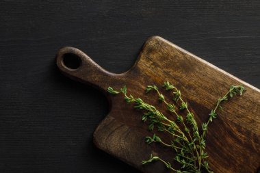 Koyu yüzeyüzerinde kekik dalları ile kahverengi ahşap kesme tahtası üst görünümü