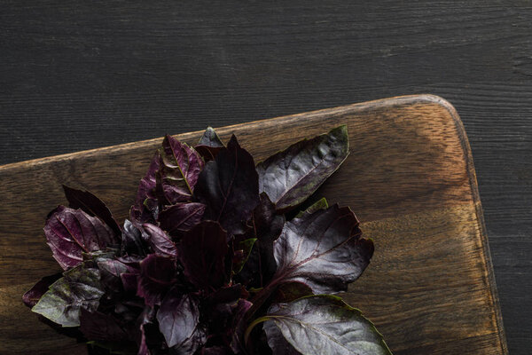 Top view of brown wooden cutting boards with purple basil bundle on dark surface