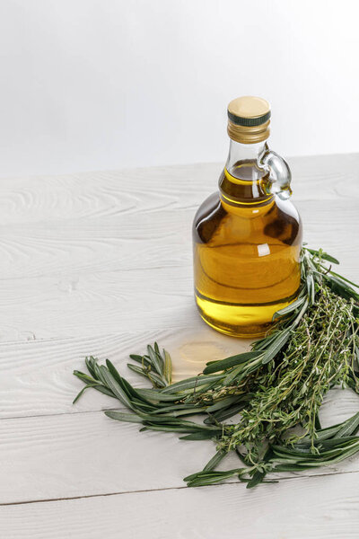 Bottle of oil near rosemary and thyme bungs on white wooden table isolated on grey
