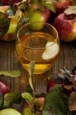 glass of fresh cider with slice near apples on wooden surface clipart