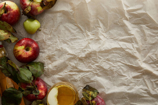 top view of apples with leaves and glass of cider on parchment paper with copy space