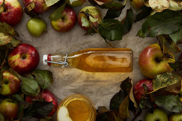 top view of bottle with cider between apples and glass with drink on parchment paper with copy space