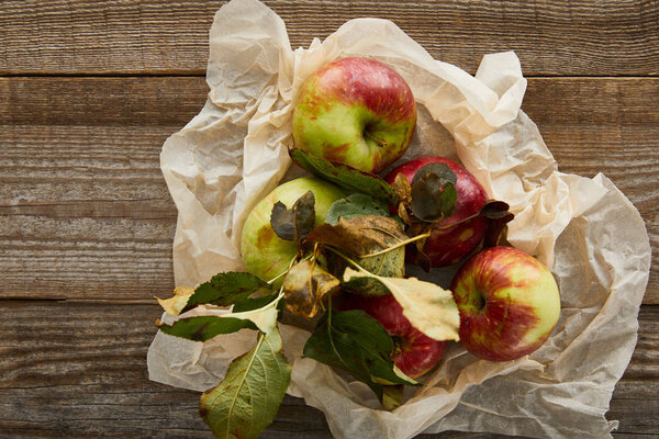 top view of ripe apples with leaves on creased parchment paper on wooden surface