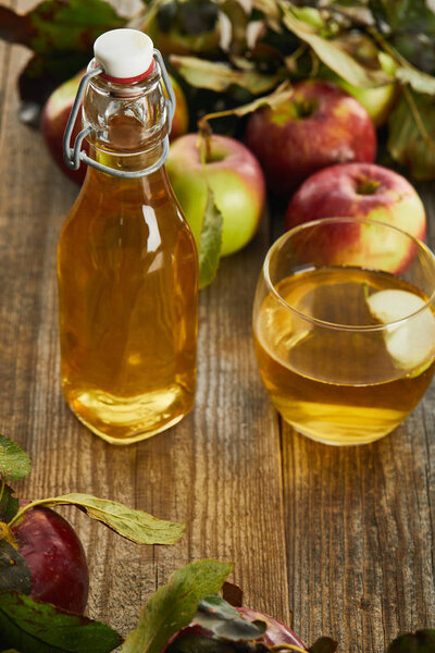 bottle of fresh cider near glass and apples on wooden surface