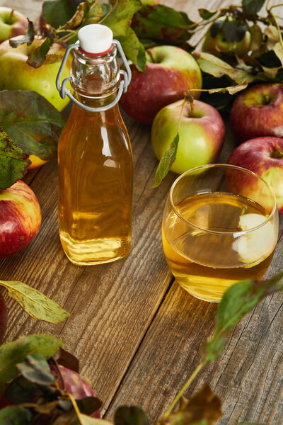 bottle and glass of fresh cider on wooden surface with ripe apples