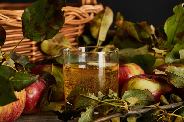 glass of cider near wicker basket and apples 