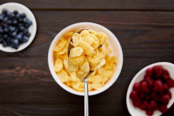 верхний вид ложки с кукурузными хлопьями над деревянной поверхностью с ягодами
