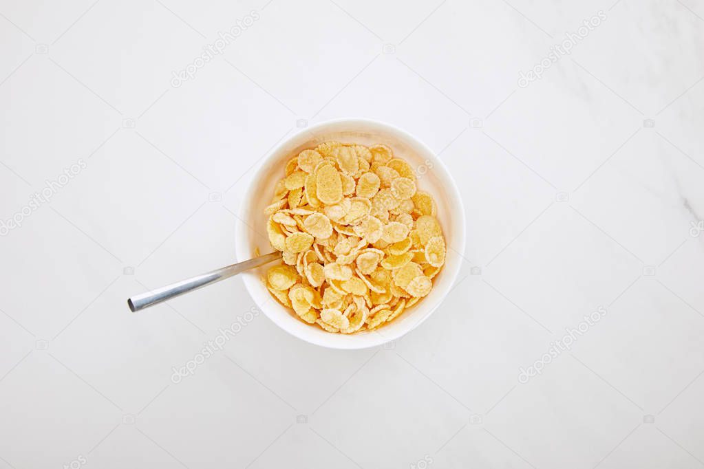 top view of bowl of cornflakes with spoon on white marble surface