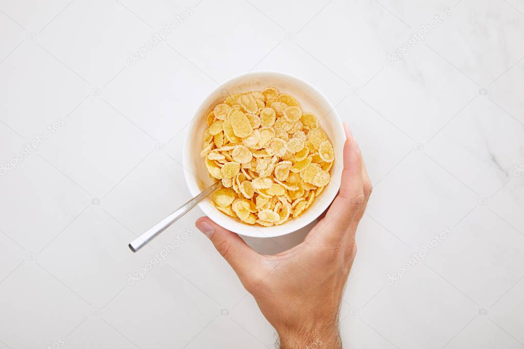cropped image of man holding white bowl with cornflakes on marble background