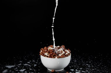 white bowl with assorted cereal with milk splashes isolated on black clipart