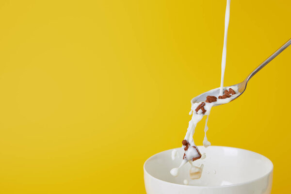 spoon with assorted cereal and milk splashes above empty bowl isolated on yellow