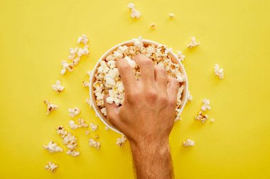 cropped view of man grabbing delicious popcorn from bucket on yellow background clipart