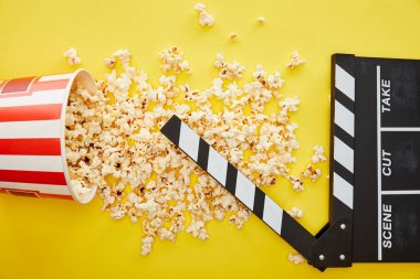 top view of delicious popcorn scattered on yellow background with clapper board clipart