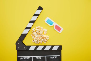 top view of crunchy popcorn near clapper board and 3d glasses on yellow background clipart
