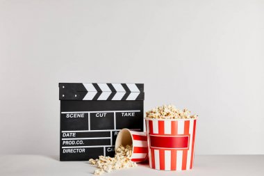 popcorn in striped buckets near clapper board isolated on grey clipart