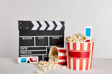 delicious popcorn scattered from buckets with clapper board and 3d glasses isolated on grey clipart